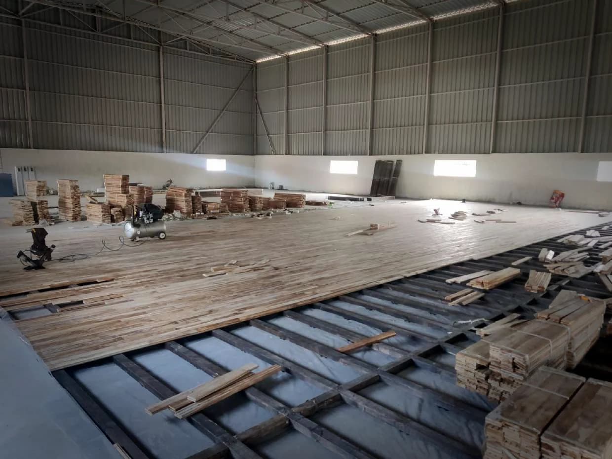 Pine members being set out across a hall floor, timber stacked alongside