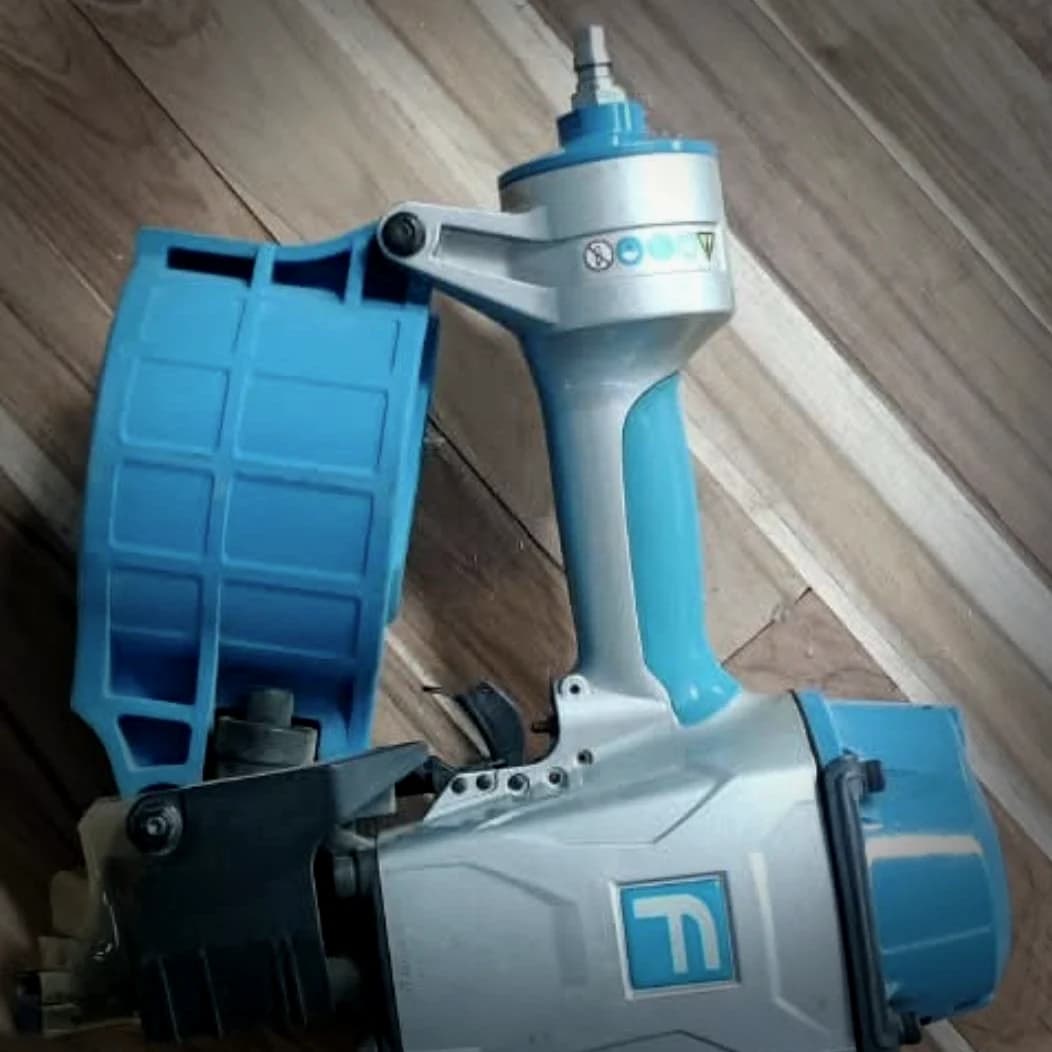 Pneumatic coil nailer with its coil magazine on the side, used to fix the interlocked pine framework