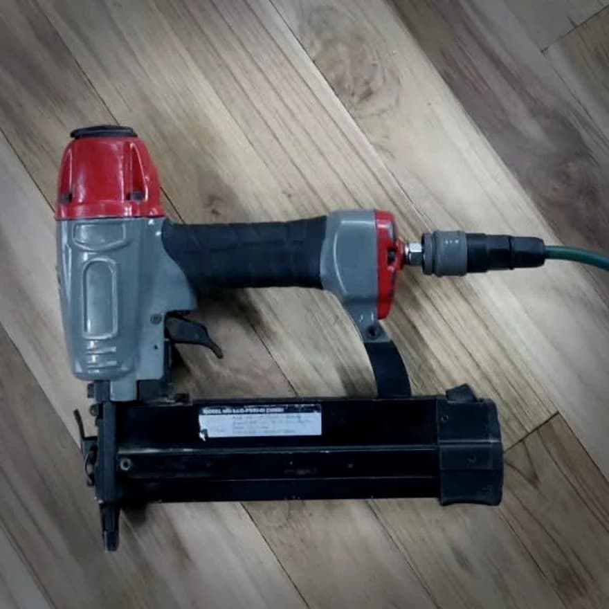 Pneumatic straight-magazine nailer, air line coupled, used to fix the shock pad rubber to the pine